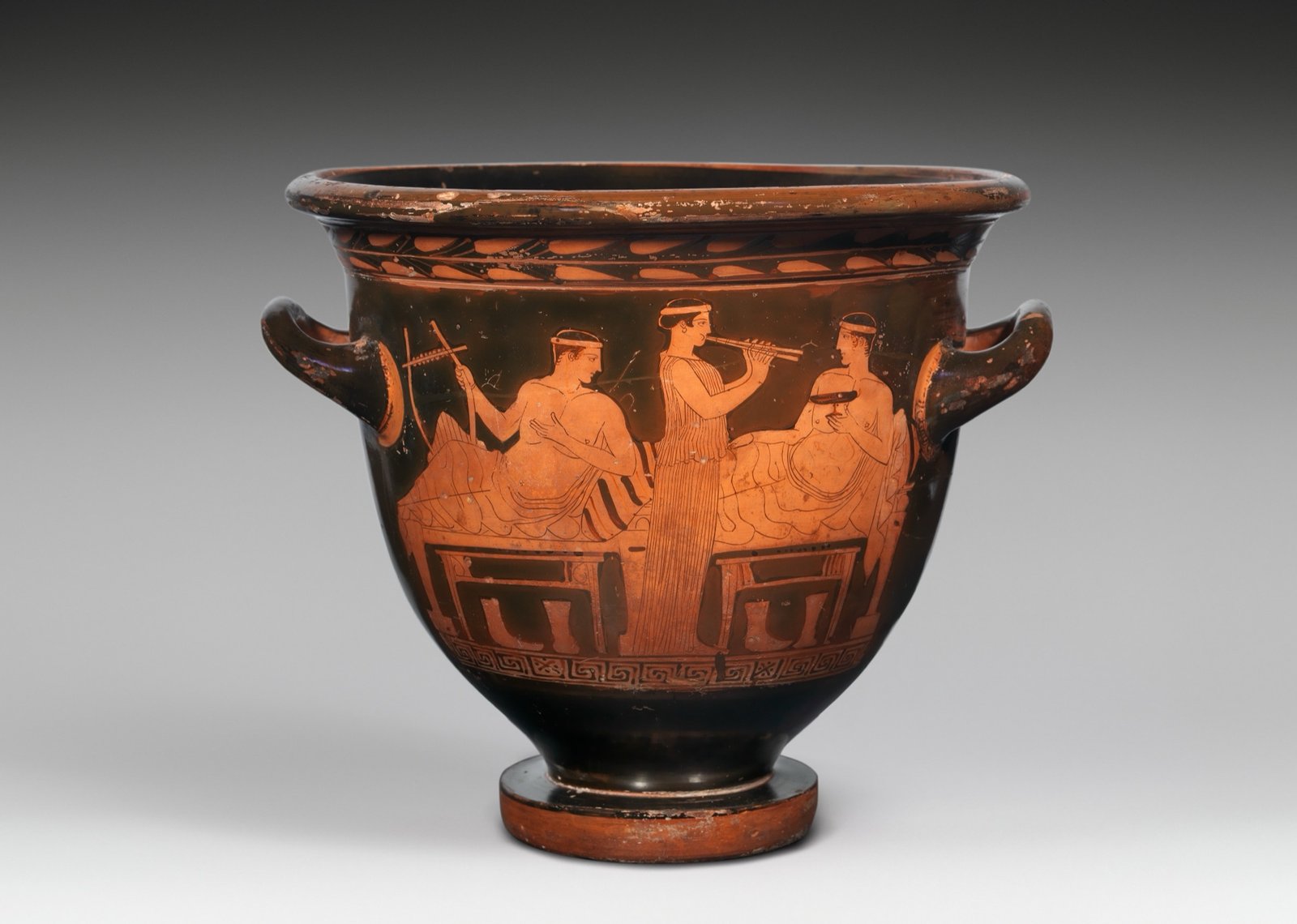 A drinking party: two men on couches, one with a lyre, one with a cup, and a woman playing the pipes between them — Athenaeus, The Learned Banqueters (Deipnosophistae)