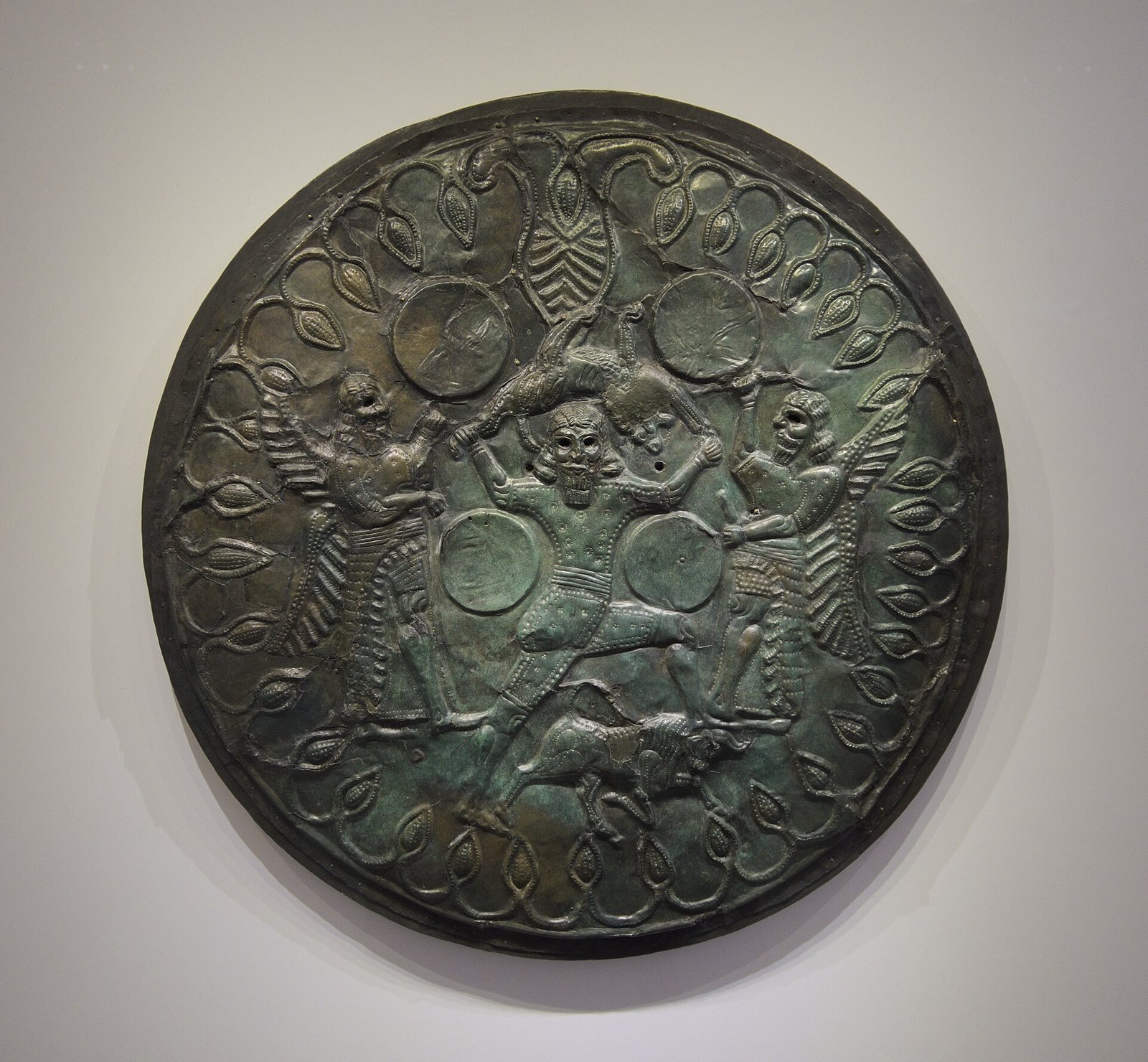 Bronze votive drum from the Idaean Cave on Crete, 8th to 7th century BC. A god, usually identified as Zeus, lifts a lion above his head between two winged figures with drums held high, often taken to be the Kouretes who guarded him as a baby in this cave.