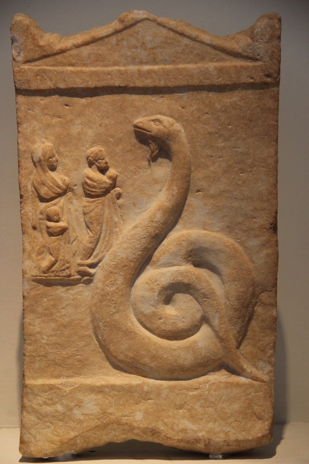 Marble offering relief found in Athens, 350 to 300 BC, given by a man named Aristomenes. Zeus Meilichios, the Gentle, appears as a great coiled snake, and a small family comes to honor him. The hymn gives the Daimon the same title, gentle Zeus.
